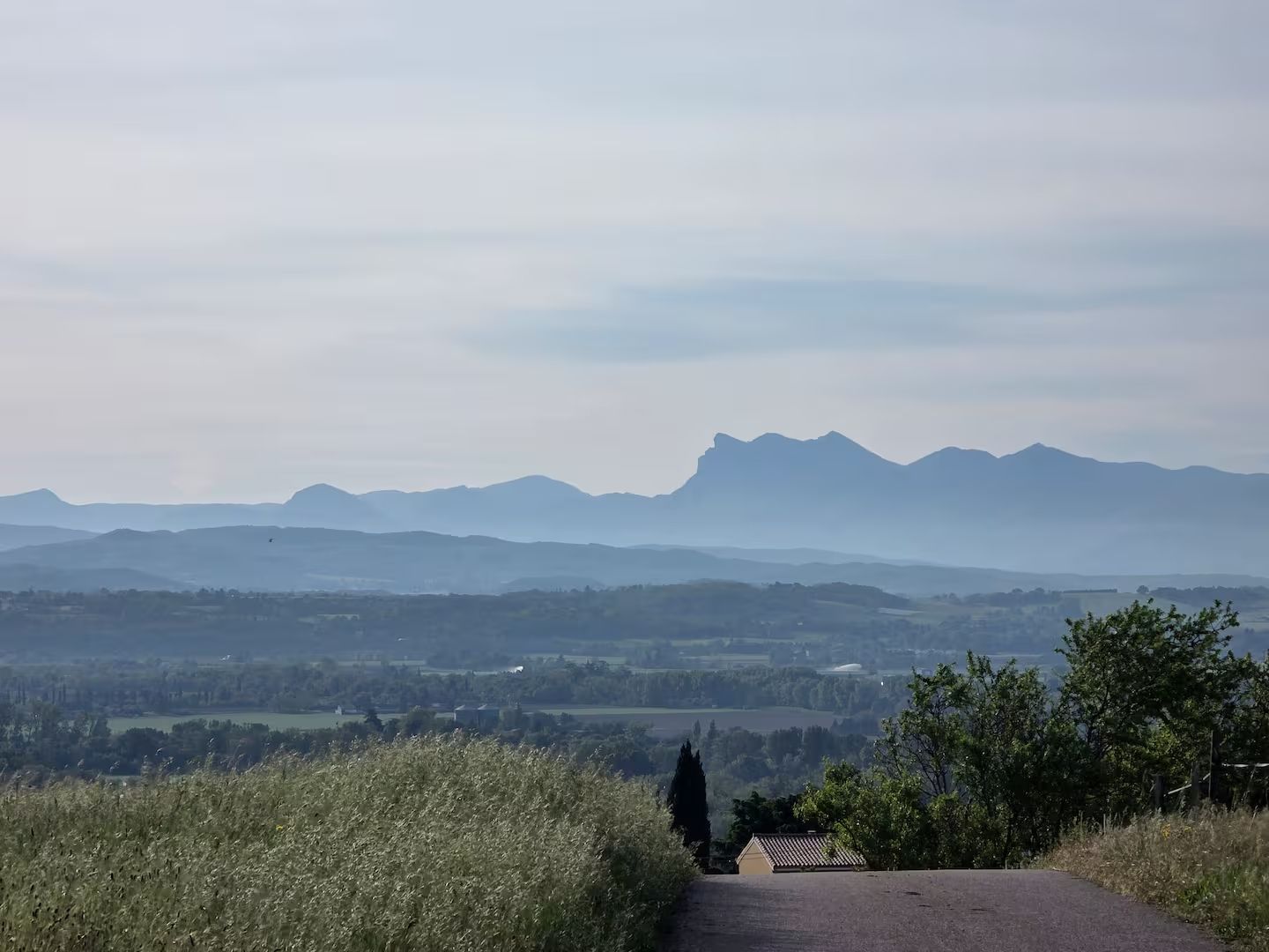Een landweg die naar een huis leidt, met uitzicht op verre bergen.