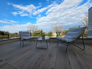 A balcony with two chairs and a small table, overlooking a landscape with trees and buildings.