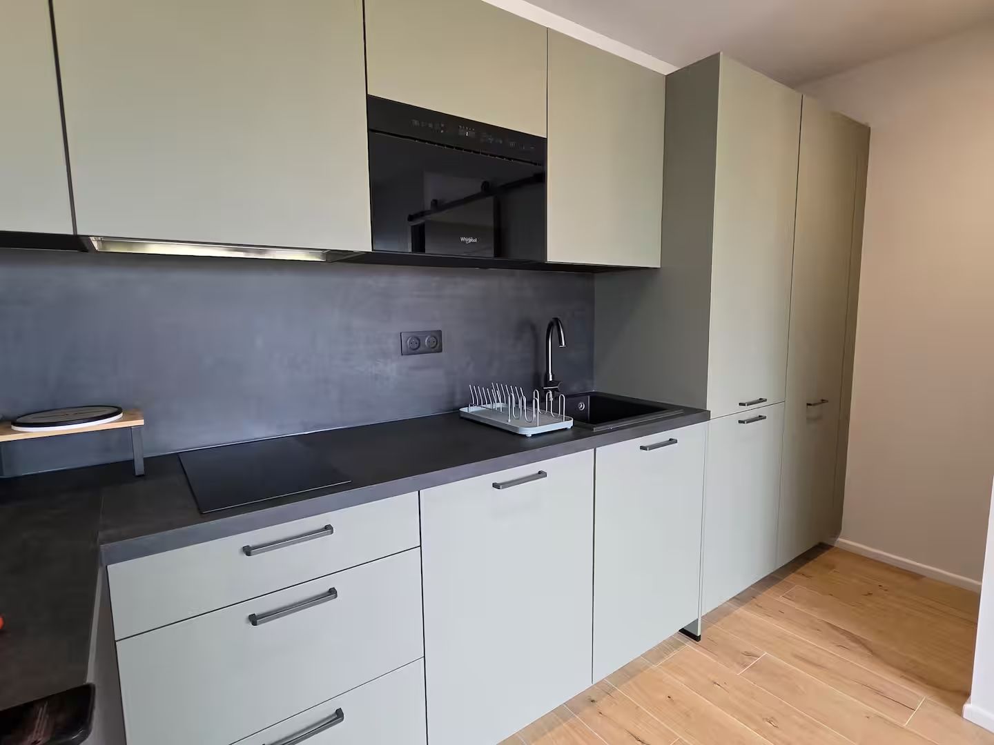 A modern kitchen with grey cabinets, a black countertop, and a built-in oven.
