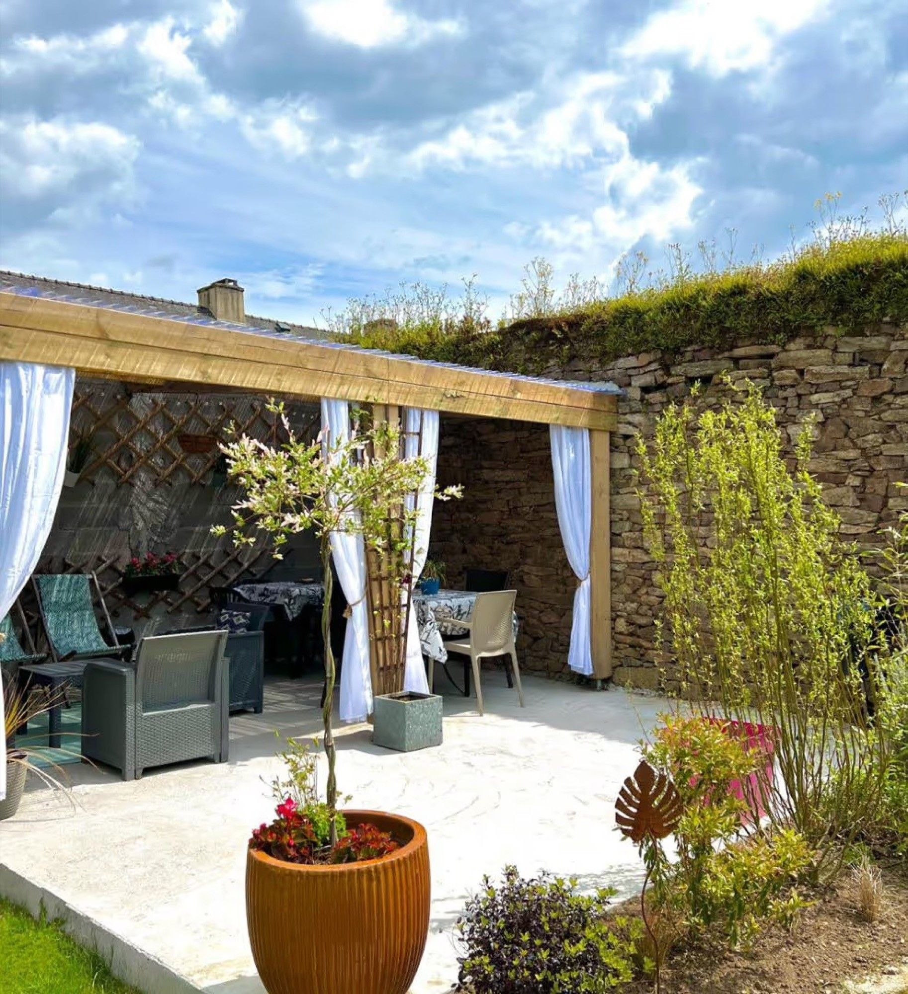 Un patio exterior con paredes de piedra, una zona de estar cubierta y plantas en macetas.