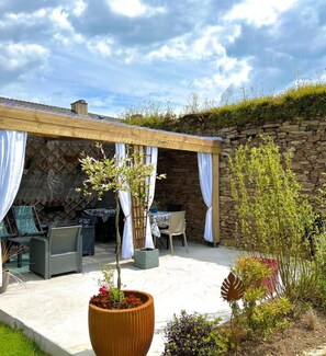 An outdoor patio with stone walls, a covered seating area, and potted plants.
