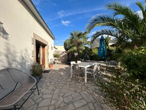 A patio with a stone floor, a white table and chairs, a wicker chair, and a wooden fence.