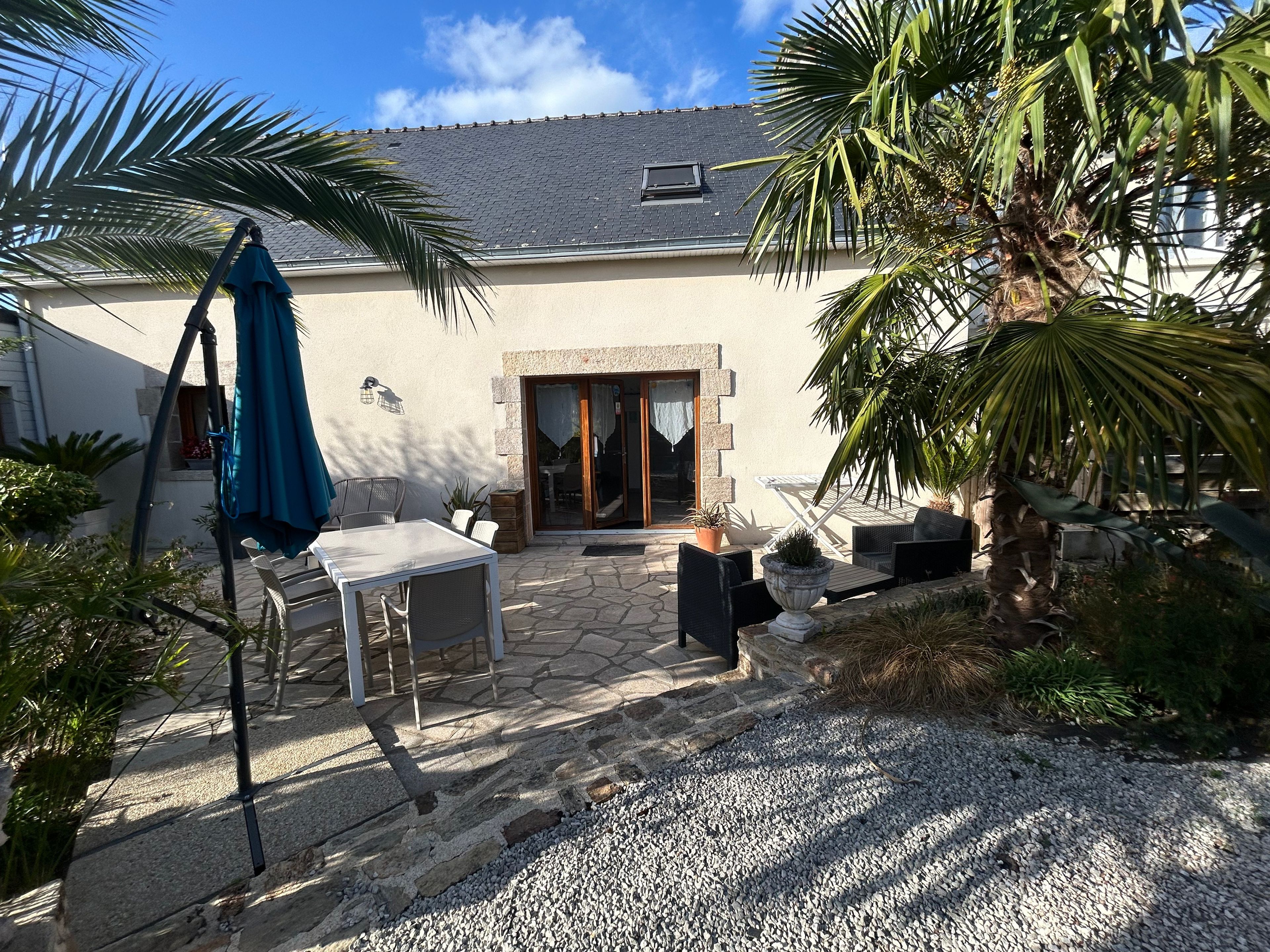 Une terrasse avec des meubles d’extérieur, un sol en pierre et un palmier.