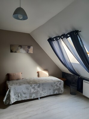 A bedroom with a sloped ceiling, a bed with patterned bedding, a wall-mounted artwork, and a window with curtains.