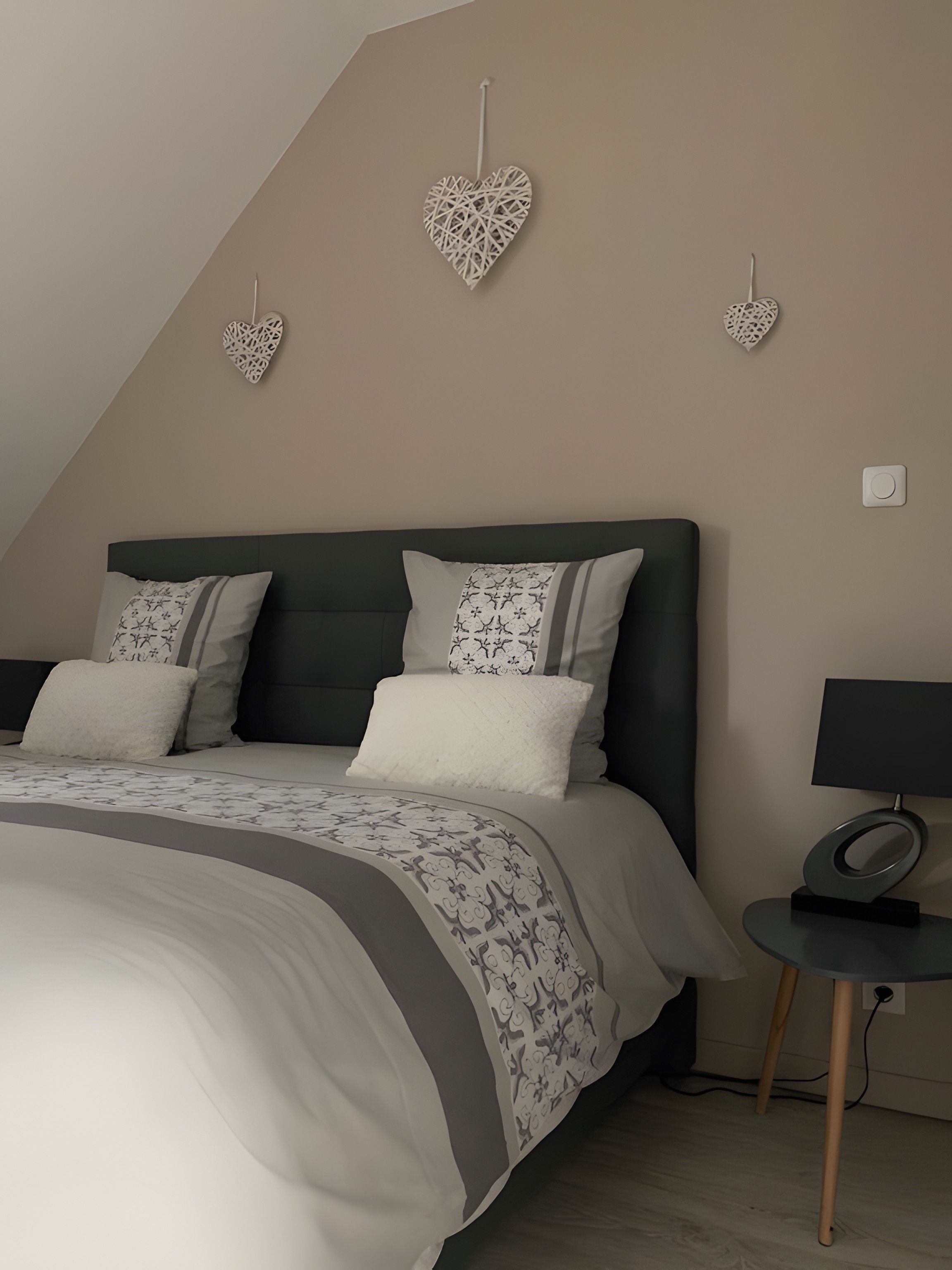 Une chambre à coucher avec un lit, des oreillers, une table de chevet avec une lampe et des décorations murales en forme de cœur.