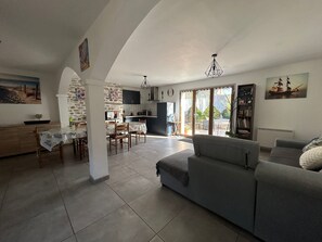 Amplia sala de estar con un sofá gris, una mesa de comedor con sillas y una cocina al fondo.