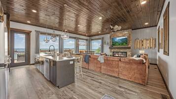 A spacious kitchen with a central island, a cozy seating area with a fireplace, and large windows offering a view of the outdoors.