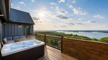 A hot tub on a wooden deck with a view of a lake and forest.