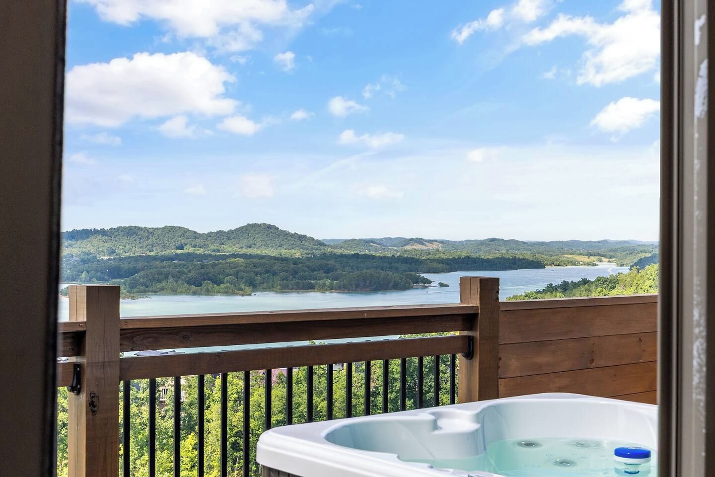 Eine Holzterrasse mit Whirlpool mit Blick auf einen See und bewaldete Hügel.