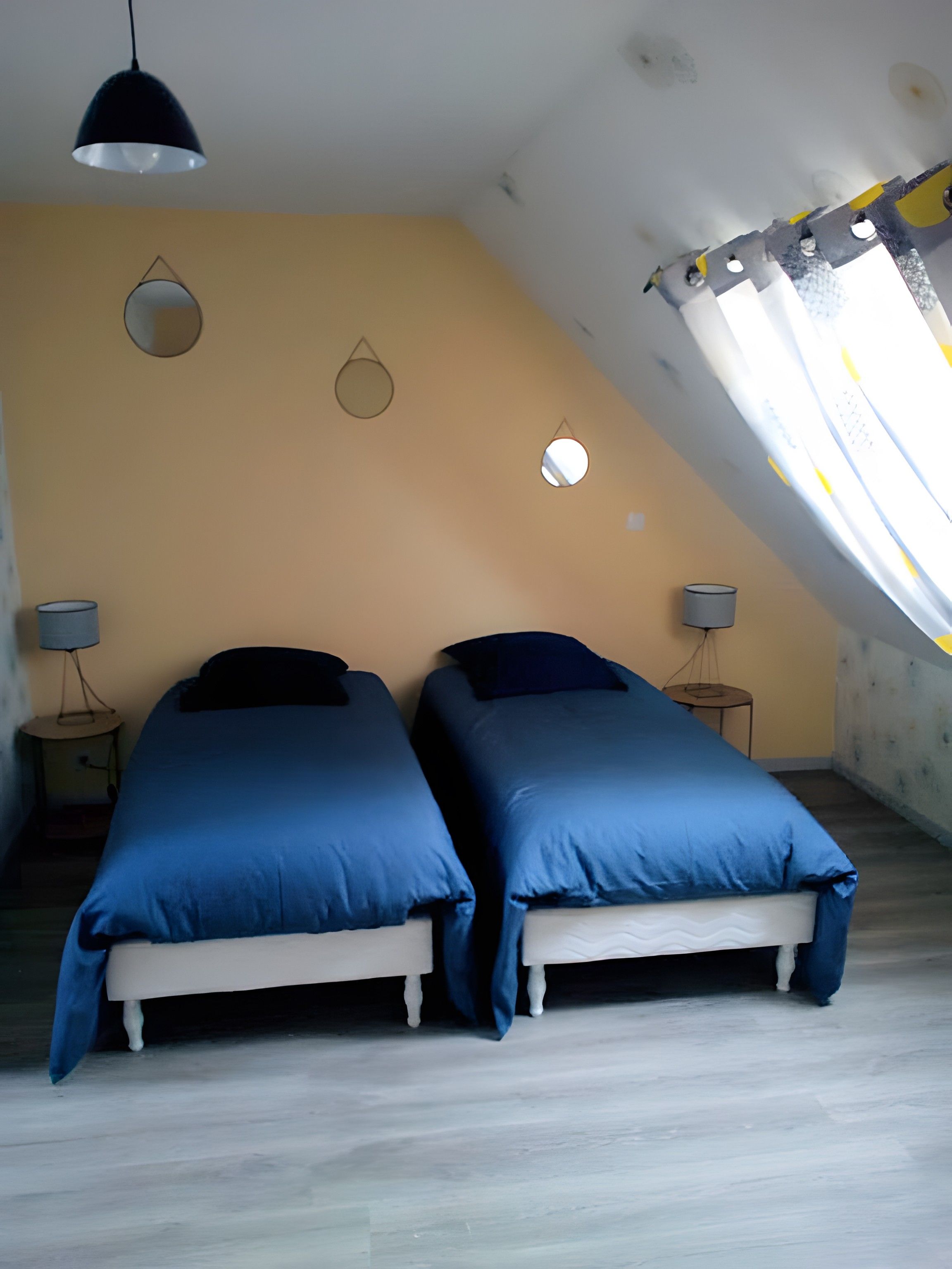 Une chambre avec deux lits, un luminaire au plafond et une fenêtre avec des rideaux.