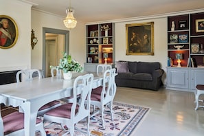Un coin repas avec une table et des chaises blanches, un lustre et une bibliothèque contenant divers objets.