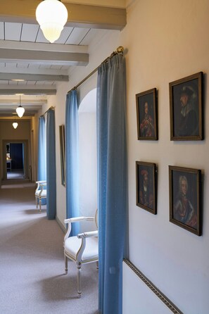 Un couloir avec une chaise, des rideaux bleus et des portraits encadrés accrochés au mur.