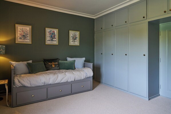 A bedroom with a bed, a wardrobe, and three framed botanical prints on the wall.