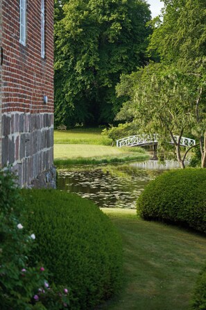 Un jardin paisible avec un étang, un pont blanc et un bâtiment en briques.