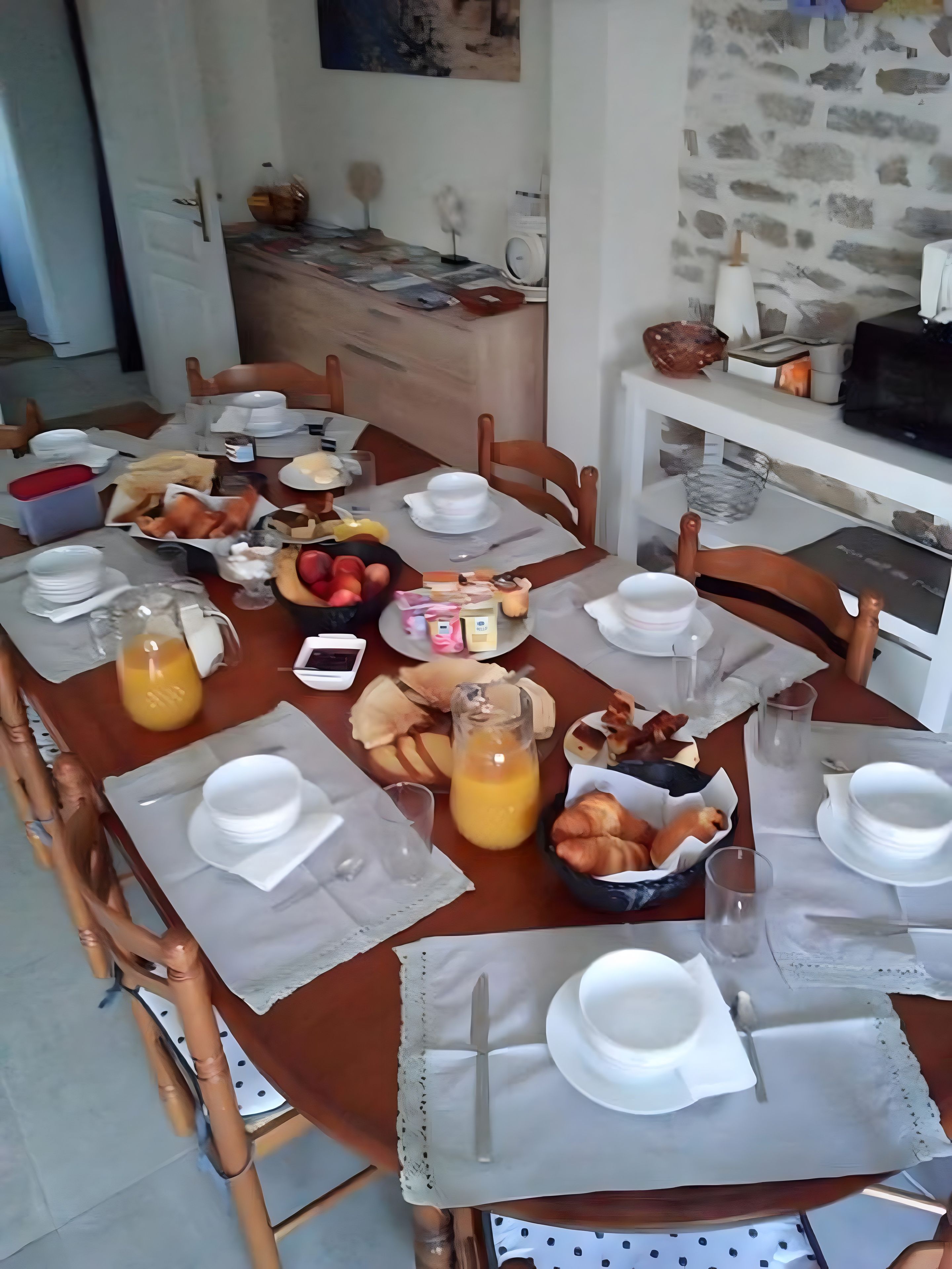 Une table à manger dressée avec des assiettes, des verres et divers aliments, ce qui indique qu’un repas va être servi.