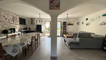 Amplia sala de estar con mesa de comedor, cocina y sofá gris.
