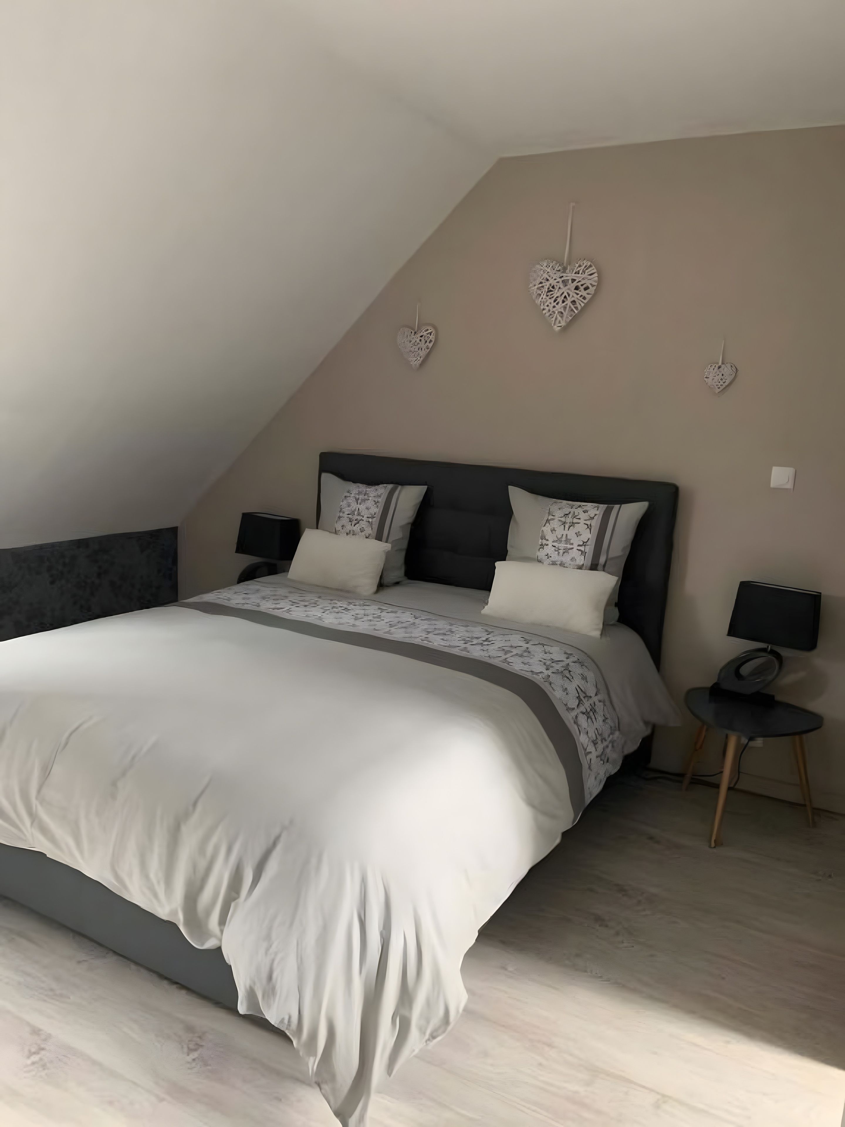 Une chambre avec un grand lit, deux tables de chevet et des décorations murales en forme de cœur.