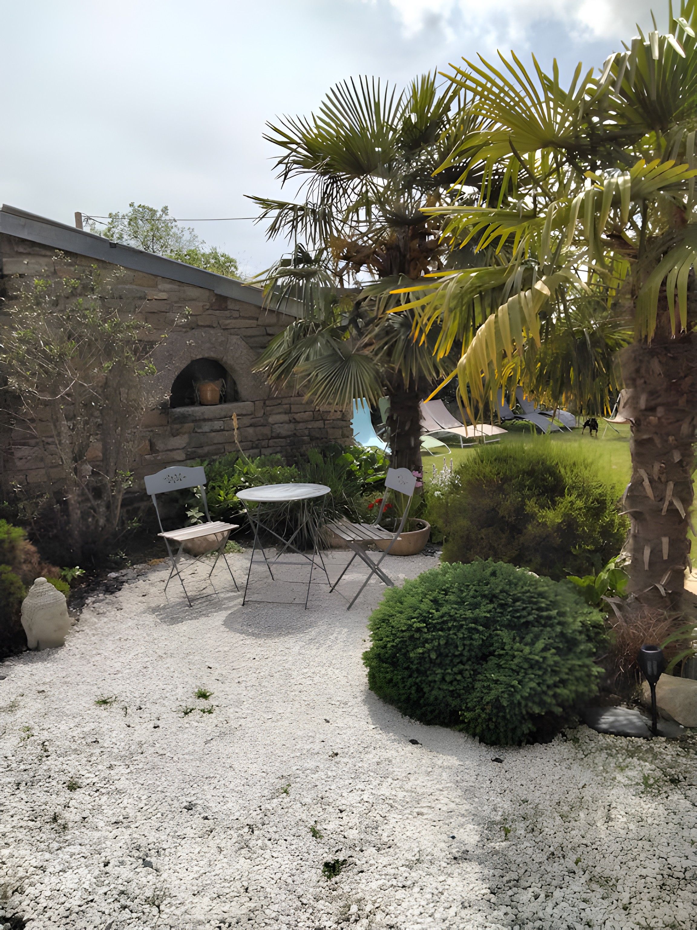 Un espace patio agrémenté d’un mur en pierre, d’une table ronde, de deux chaises et d’un palmier.