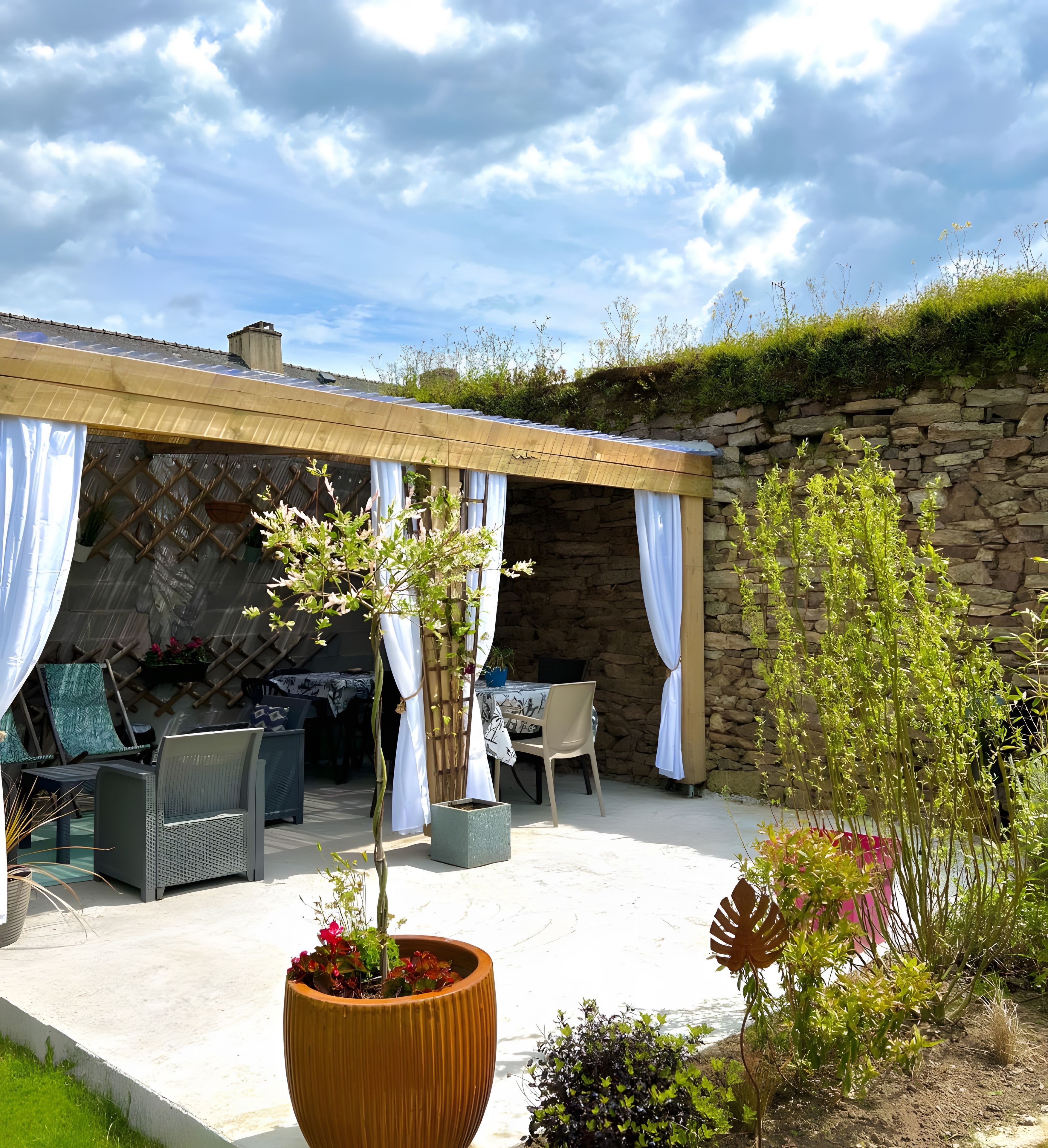 Un espace extérieur aménagé en patio, avec un mur en pierre, des sièges abrités et des plantes en pot.