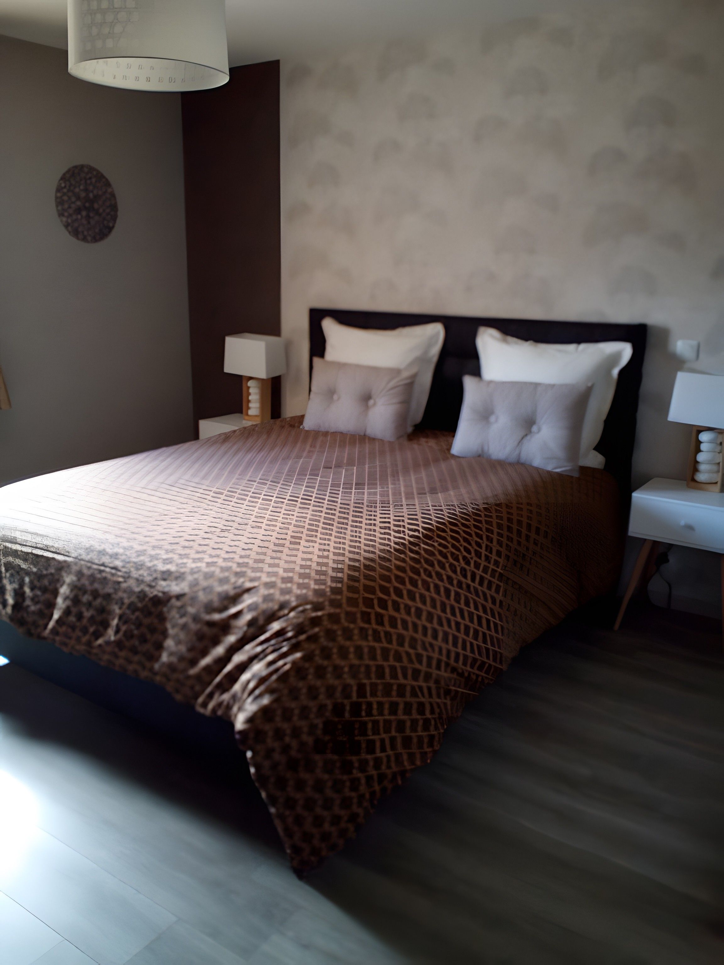 A hotel room with a bed, bedside tables, and a wall-mounted lamp.