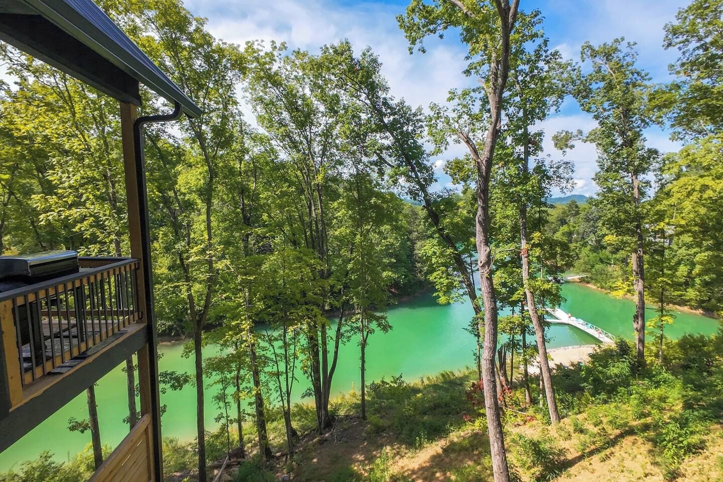 A view from a wooden deck overlooking a green river with a bridge, surrounded by trees.