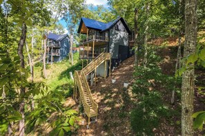 Eine mehrstöckige Holzdiele mit Balkon, umgeben von Bäumen und einer Holztreppe, die zu den oberen Ebenen führt.
