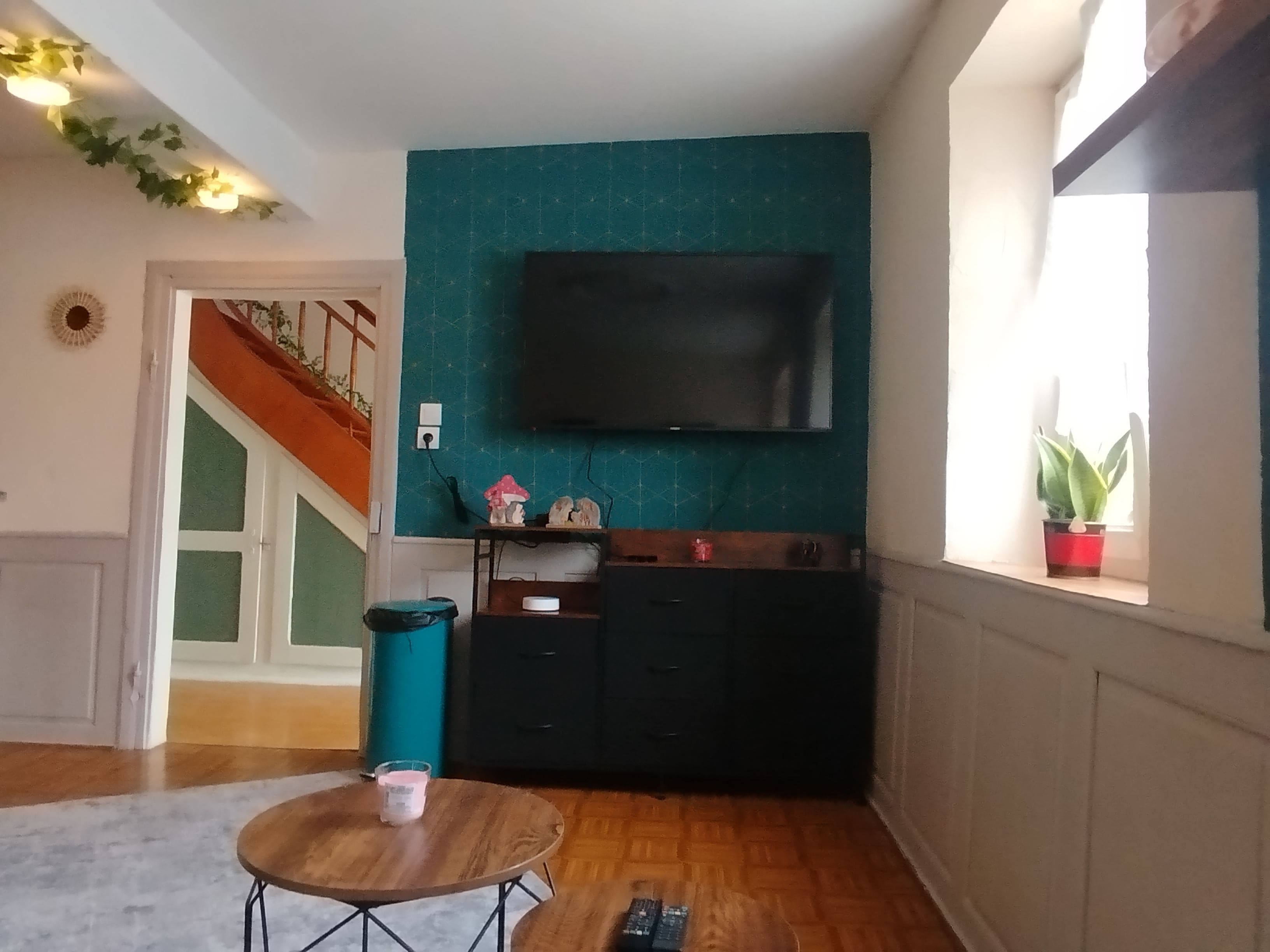 Un salon avec un mur d’accent de couleur turquoise, un téléviseur à écran plat, un meuble en bois et une petite table avec une télécommande.