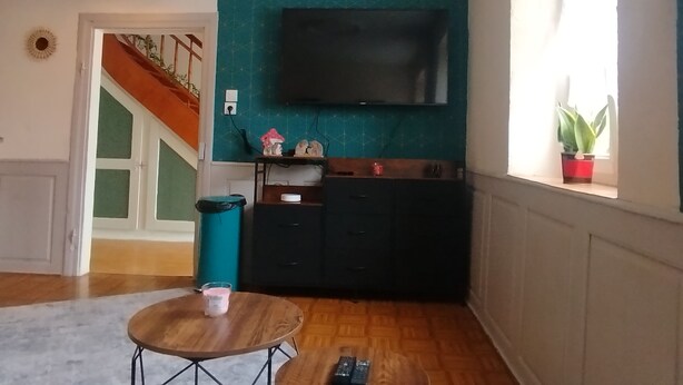 A living room with a teal accent wall, a flat-screen TV, a wooden cabinet, and a small table with a remote control. - The Great Cozy Safari (Petersbach)