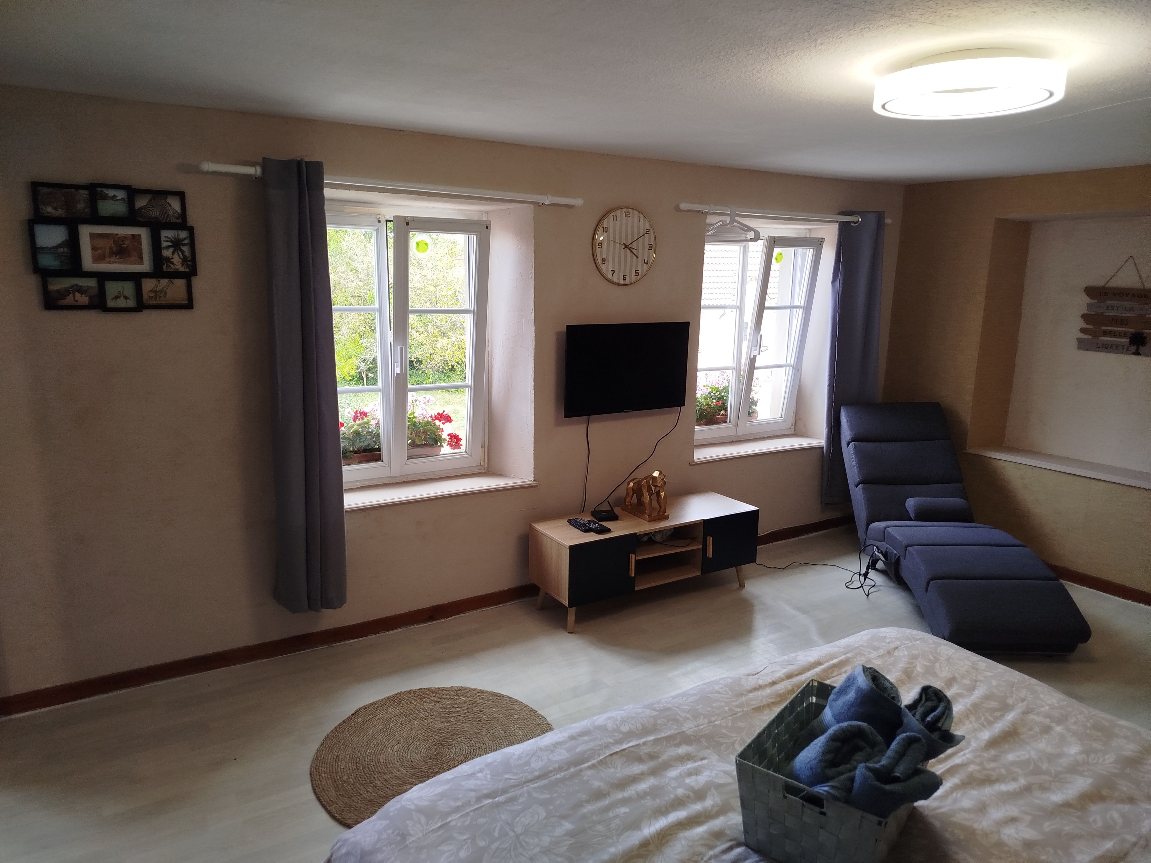 Une chambre à coucher avec un lit, un bureau avec une télévision, une chaise et des fenêtres avec des rideaux.
