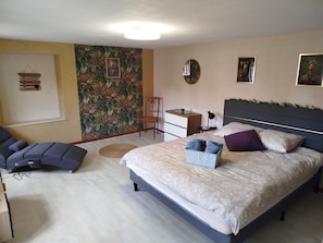 A bedroom with a bed, a desk, a chair, and a wall with a tropical wallpaper. - The Great Cozy Safari (Petersbach)
