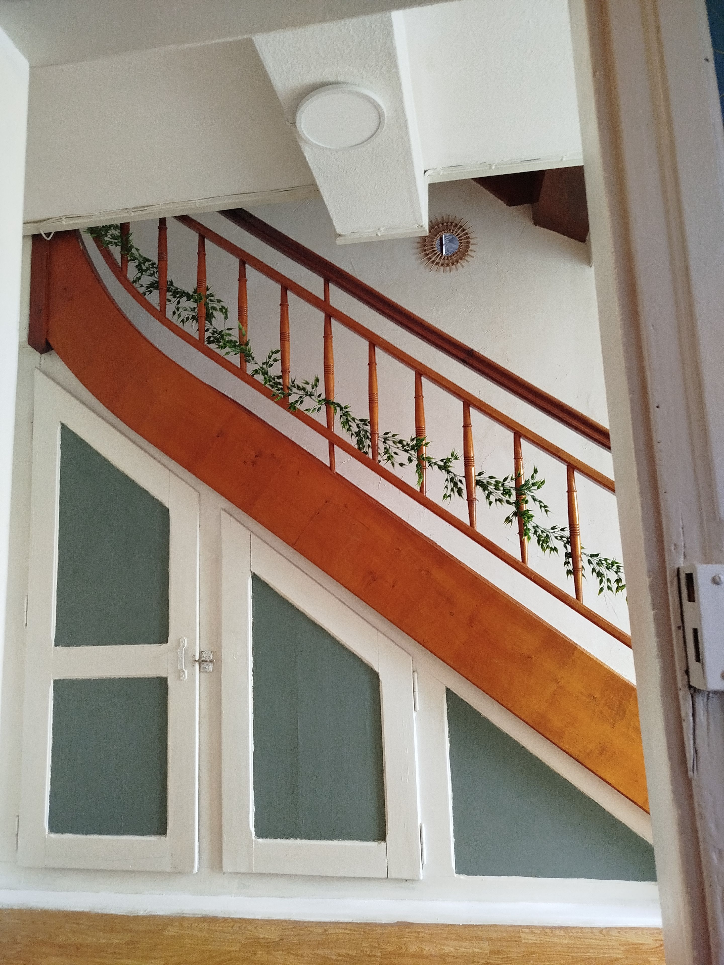 Un escalier avec une rampe en bois et un mur blanc orné d’une plaque décorative.