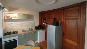 A compact kitchen with a stove, sink, and refrigerator, wooden cabinets, and a herringbone-patterned backsplash. - The Great Cozy Safari (Petersbach)