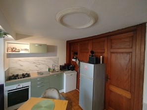 A compact kitchen with a stove, sink, and refrigerator, wooden cabinets, and a herringbone-patterned backsplash. - The Great Cozy Safari (Petersbach)