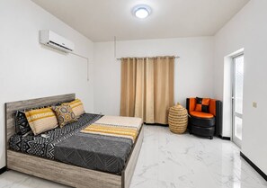 Ein Schlafzimmer mit einem Bett, einem Fenster, einem Sessel und einer Klimaanlage.