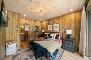 A wooden-paneled bedroom with a bed, bedside tables, a window, and a door leading to a bathroom. - Private Dock-Lakefront-Views-Pets-Beach Access (Sevierville)