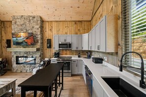 A modern kitchen with a stone fireplace, wooden ceiling, and a large window with blinds. - Private Dock-Lakefront-Views-Pets-Beach Access (Sevierville)