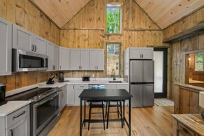 Una cocina con paredes de madera, un refrigerador de acero inoxidable, un microondas y una estufa.