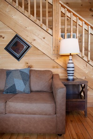 A wooden staircase with a handrail, a brown leather sofa with a patterned pillow, and a table with a lamp and a vase. - Radiant Sky Views | Hot Tub, Game Room, MORE! (Sevierville)