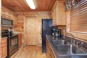 A wooden cabin interior with a kitchen featuring a microwave, stove, refrigerator, and a coffee maker. - Radiant Sky Views | Hot Tub, Game Room, MORE! (Sevierville)