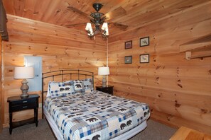 A wooden-paneled bedroom with a bed, two bedside tables with lamps, a ceiling fan, and framed pictures on the wall. - Radiant Sky Views | Hot Tub, Game Room, MORE! (Sevierville)