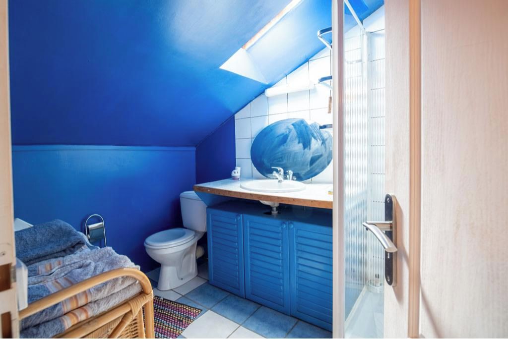 A compact bathroom with a blue wall, a white toilet, a sink, and a shower area.