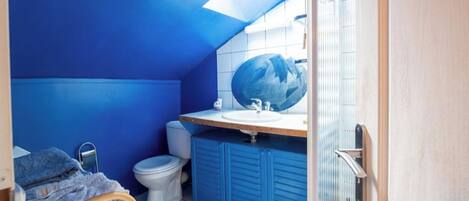 A compact bathroom with a blue wall, a white toilet, a sink, and a shower area.