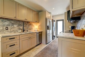 A modern kitchen with marble countertops, stainless steel appliances, and beige cabinetry. - Cozy Sarasota Bungalow + Tropical Outdoor Space (Sarasota)