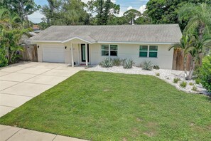 A single-story house with a garage, a well-maintained lawn, and a variety of plants. - Cozy Sarasota Bungalow + Tropical Outdoor Space (Sarasota)