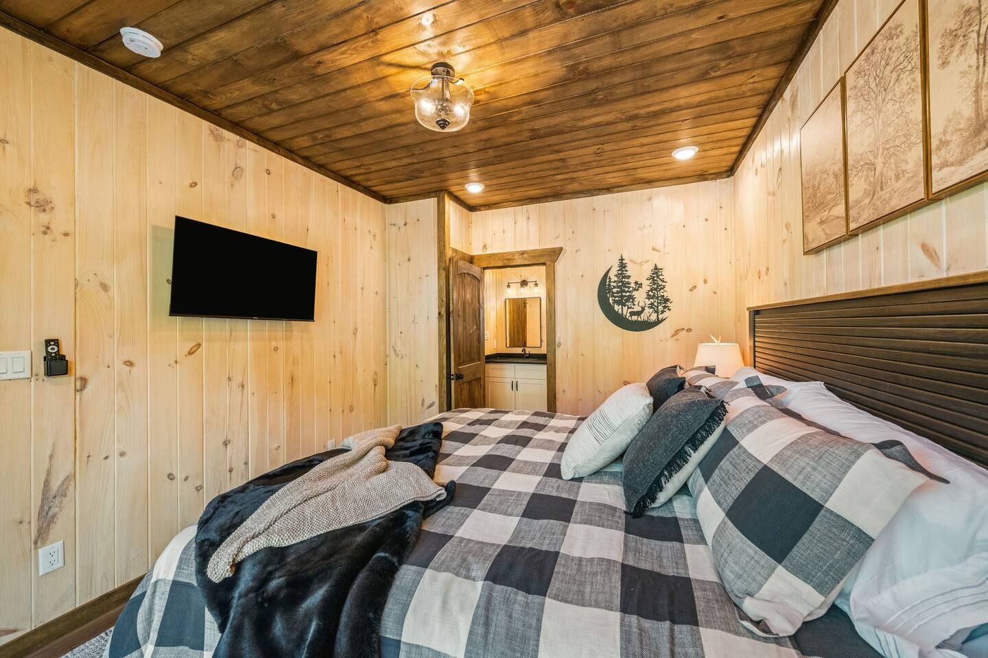Ein Zimmer mit Holzvertäfelung, einem Bett, einem an der Wand befestigten Fernseher und einer Tür zu einem Badezimmer.