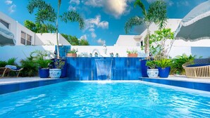 A swimming pool with a waterfall feature, surrounded by potted plants and a white building. - Casa Azul - Your Own Private Boutique Hotel for 12 - Breakfast Included (San Juan)