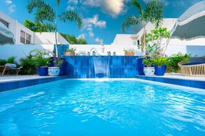 A swimming pool with a waterfall feature, surrounded by potted plants and a white building. - Casa Azul - Your Own Private Boutique Hotel for 12 - Breakfast Included (San Juan)