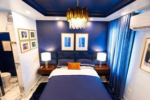 A bedroom with a large bed, two bedside tables with lamps, a chandelier, and artwork on the walls. - Casa Azul - Your Own Private Boutique Hotel for 12 - Breakfast Included (San Juan)