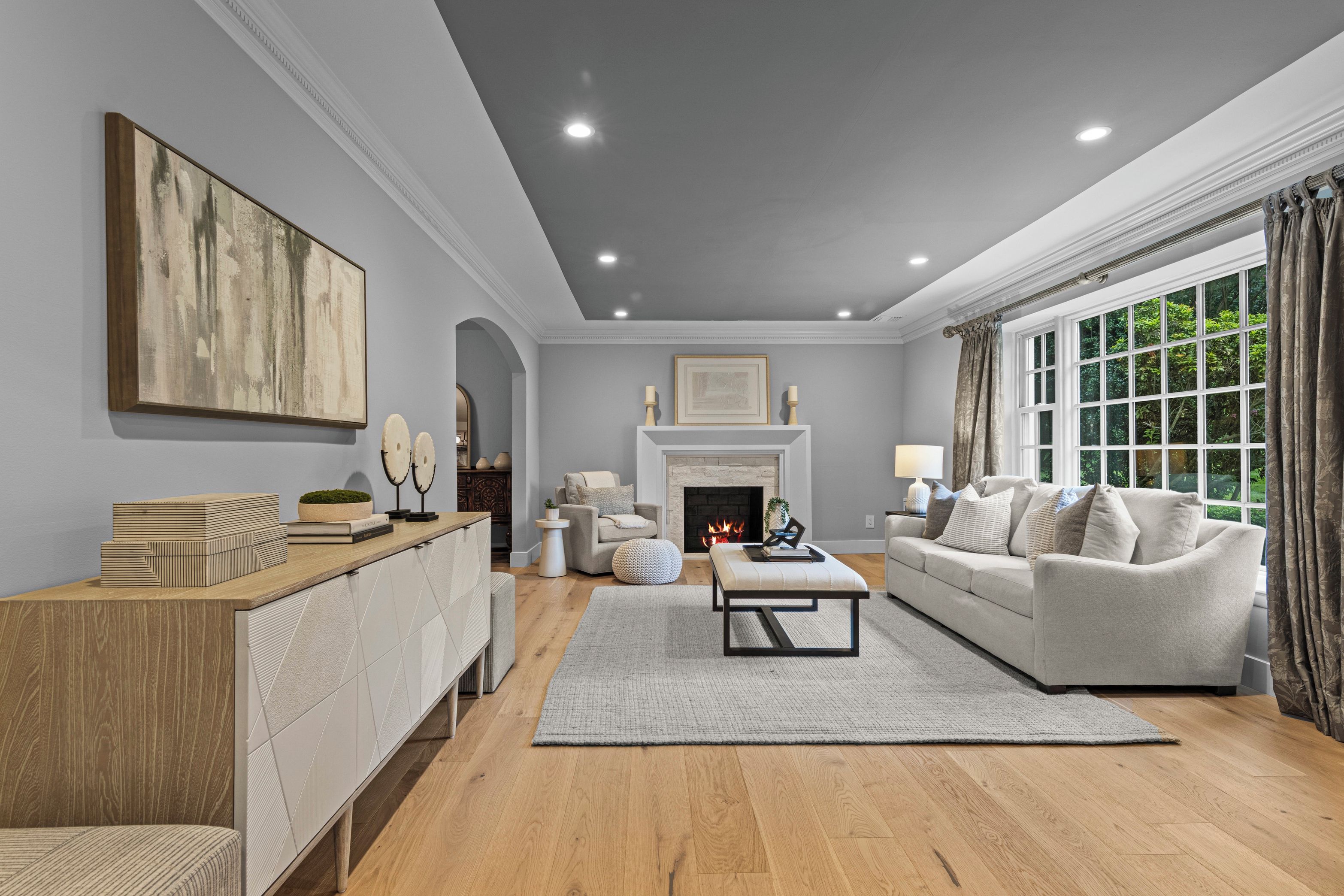 A spacious living room with a fireplace, a sofa set, a coffee table, and a large window with curtains.