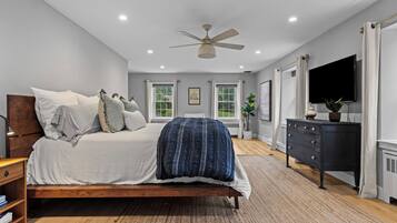 A bedroom with a bed, a ceiling fan, a dresser, a TV, and windows.